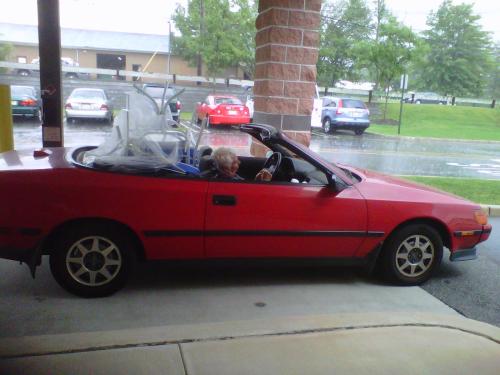 red convertible, raining, caught in the rain, top down, lawn furniture